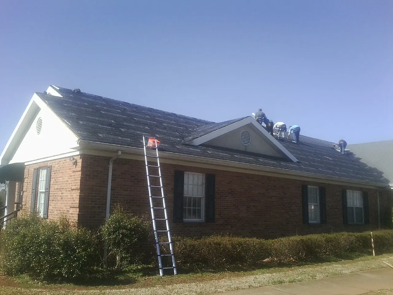 Crew tearing shingles off a brick ranch roof with a ladder set — Emergency Roof Repair work by our crew in Elkridge