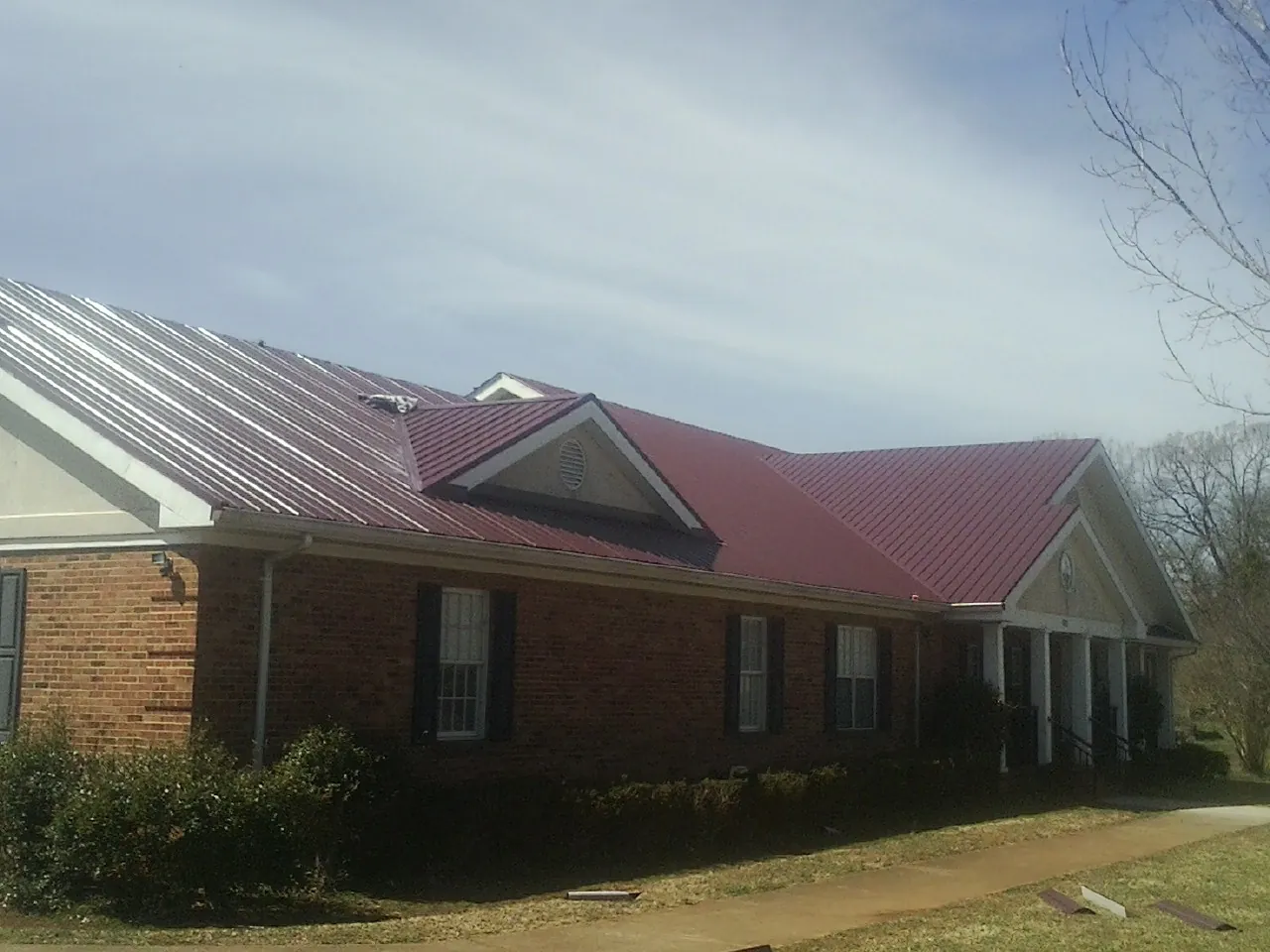 Red metal roof with gabled entries on a long brick building, from a Hail Damage Roof Repair job in Elkridge