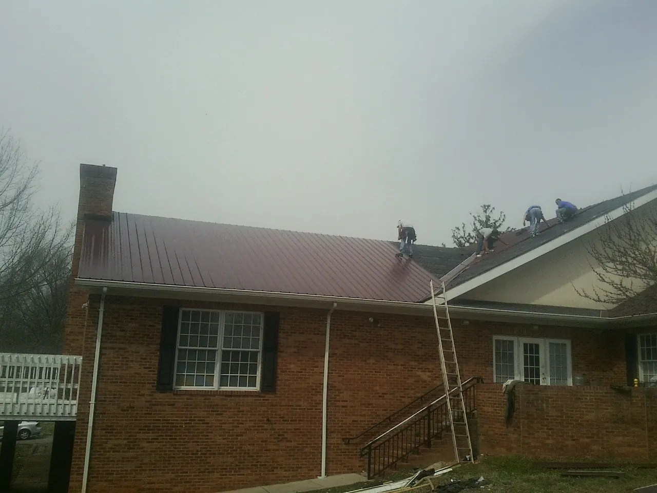 Crew setting red metal roofing panels on a brick home in Elkridge