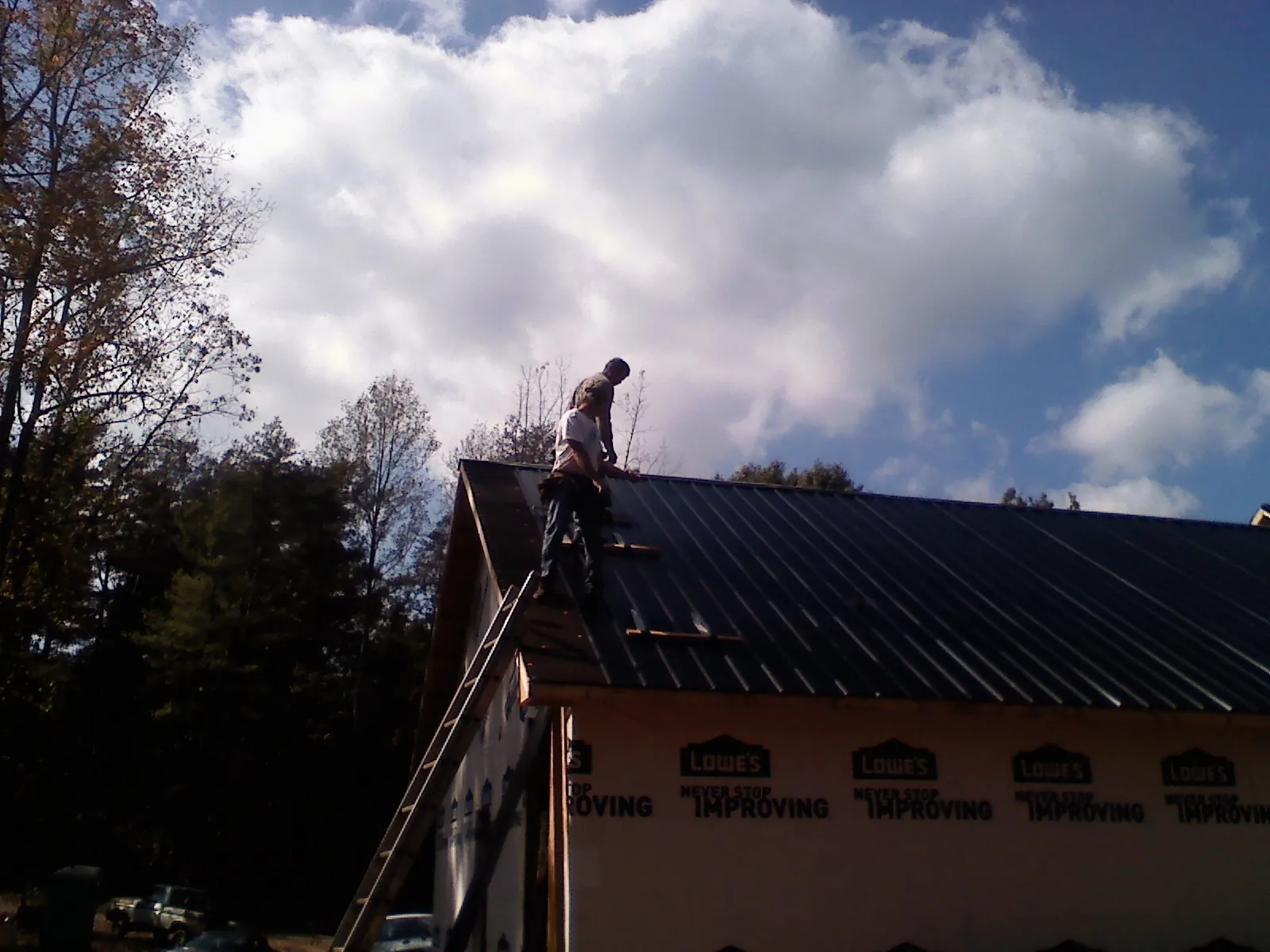 Roofer fastening dark metal panels high against a cloudy sky, from a Roof Inspection job in Elkridge