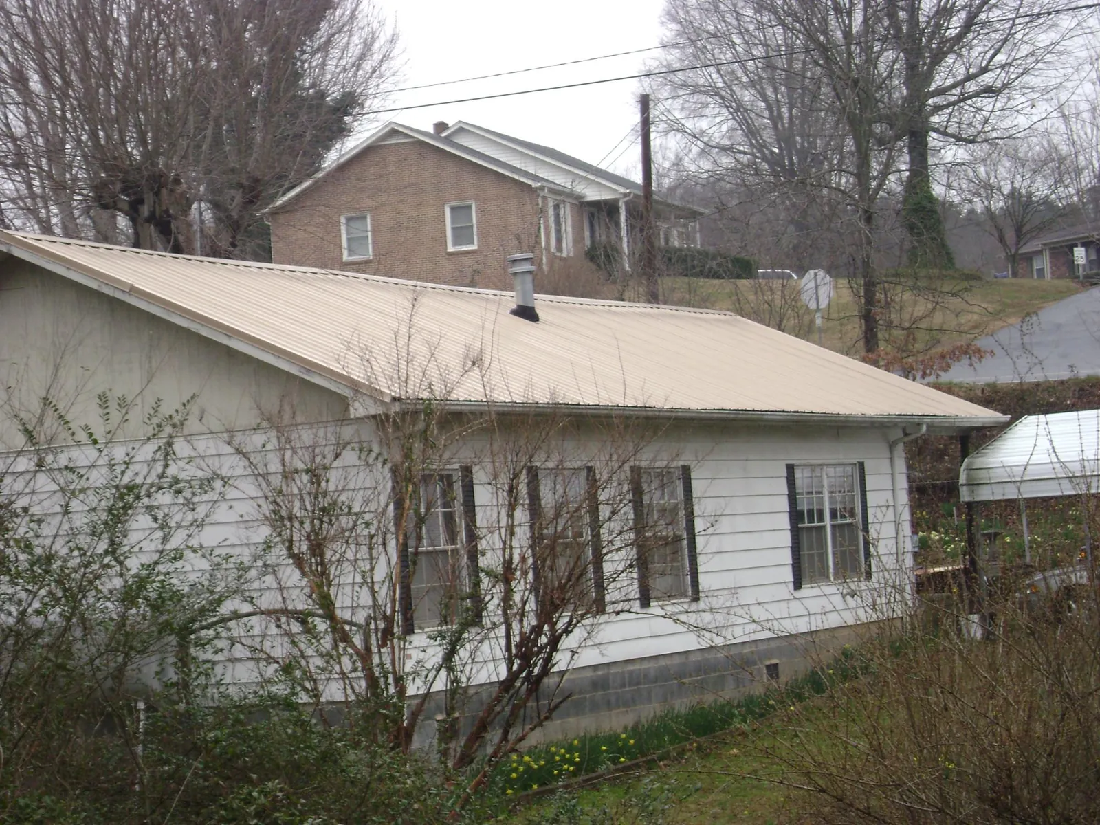 Tan metal roof on a white sided house set into a hillside — Commercial Roofing by Roofing Brothers in Elkridge